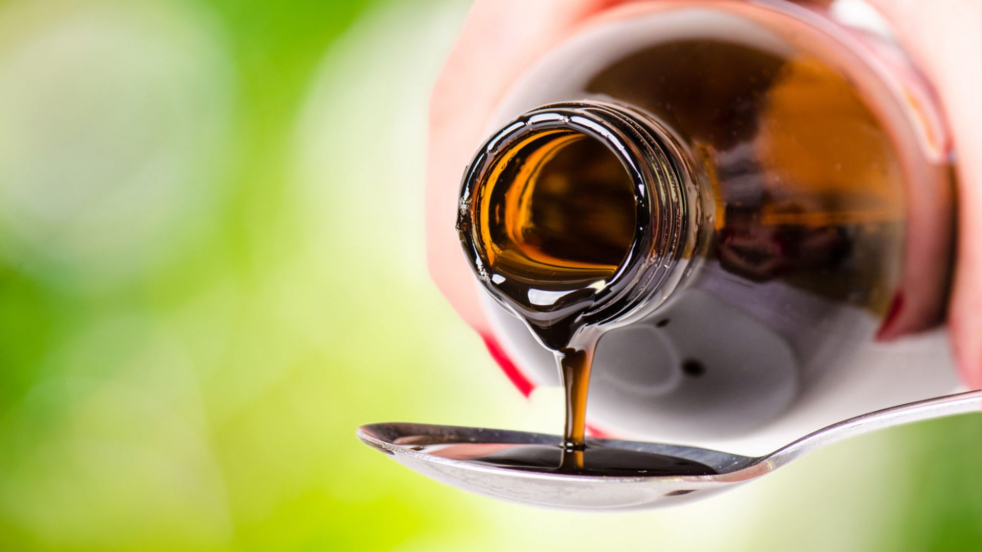 pouring a liquid on a spoon. Natural green background. Pharmacy and healthy background. Medicine. Cough and cold drug.